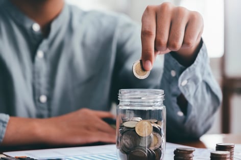 A person sitting at a table counting coins from out of a jar. 